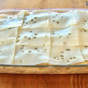 Baking dish of stove top stuffing casserole topped with slices of Swiss cheese.
