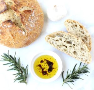 Bread dipping oil in small dish with slices of bread and bread loaf.