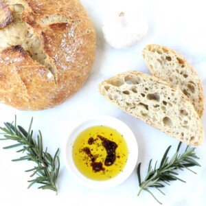 Bread dipping oil in small dish with slices of bread and bread loaf.