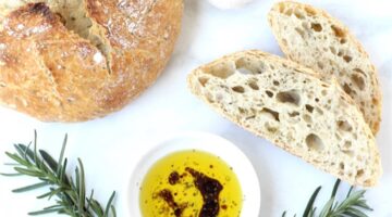 Bread dipping oil in small dish with slices of bread and bread loaf.