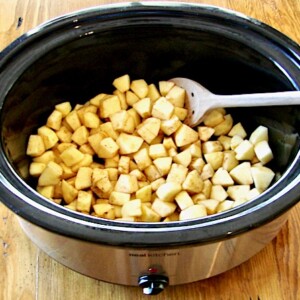Wooden spoon stirring apple pieces in a slow cooker.