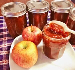 Spoon in a jar of Apple Butter with apples.