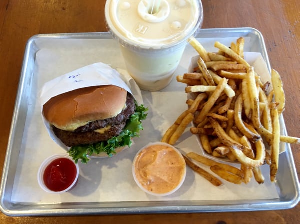 Burger, fries and milkshake on tray with sauce on the side.