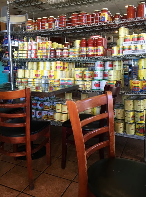 Racks of cans on a grocery aisle with tables and chairs for dining.