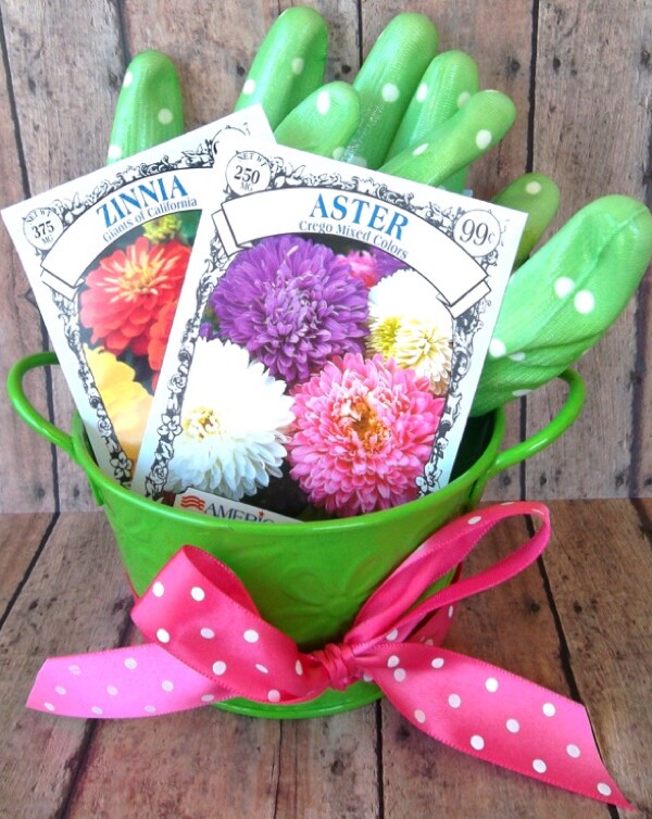 Flower seeds and gardening gloves in a green pail tied with a pink ribbon.