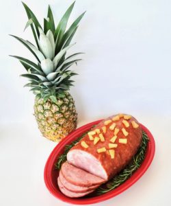 Ham on a platter next to a pineapple.