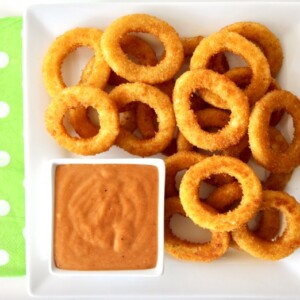Onion rings on a plate with a red dip.