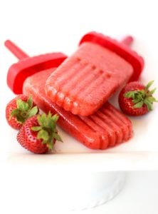 Two strawberry popsicles next to strawberries.