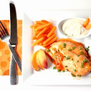 Peach chicken on a plate with carrots and dip.