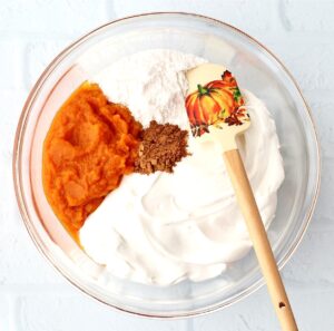 Pumpkin dip ingredients unmixed in a bowl with a spatula.