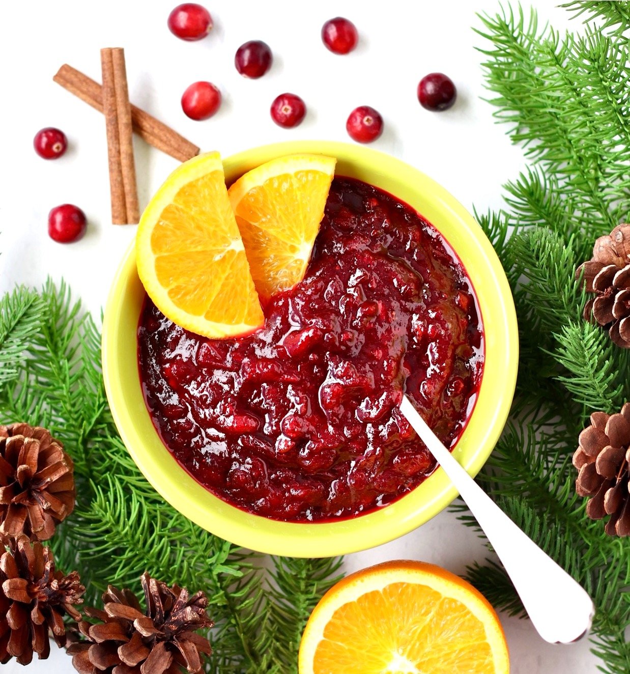 Cranberry sauce in yellow bowl with spoon and orange slices.