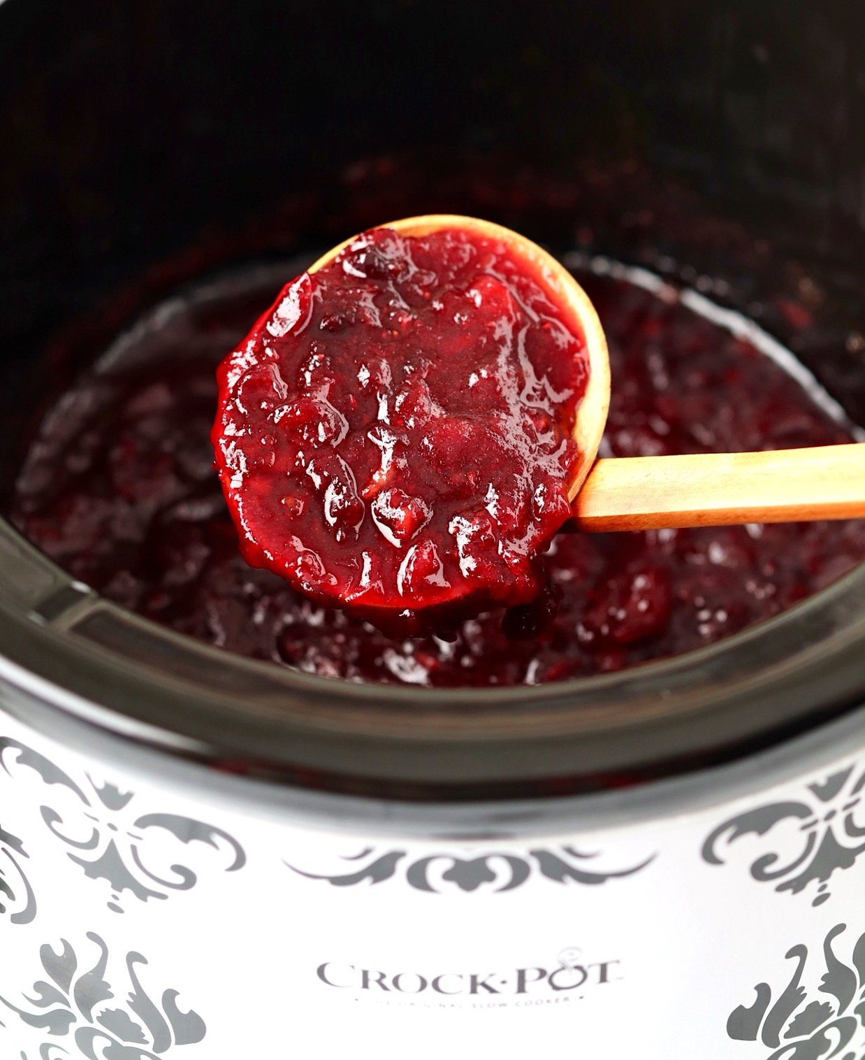 Cooked cranberry sauce on ladle with slow cooker in the background.