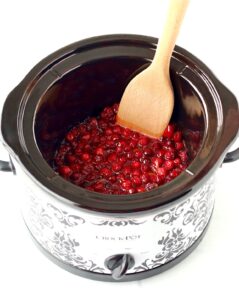 Cranberry sauce in slow cooker with wooden spatula.