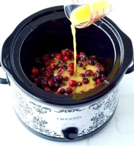 Crockpot cranberry sauce in slow cooker with orange juice being poured in.