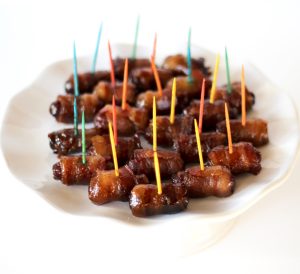 Bacon-wrapped smokies with toothpicks on a plate.