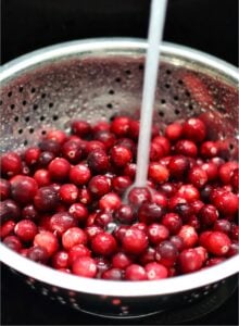 Cranberries being rinsed with water in colander.