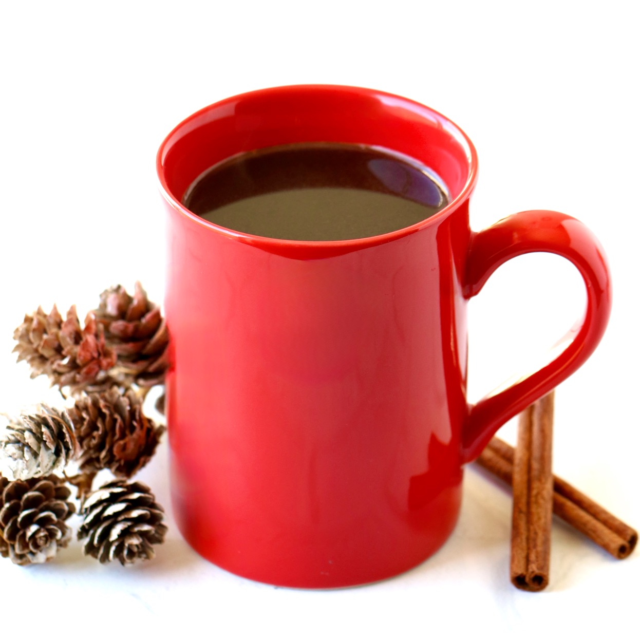 Christmas coffee in red mug with small pinecones and cinnamon sticks to the side.