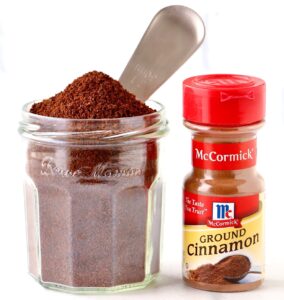 Coffee grounds in jar with coffee scoop and ground cinnamon.