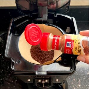 Person adding cinnamon to a coffee maker.