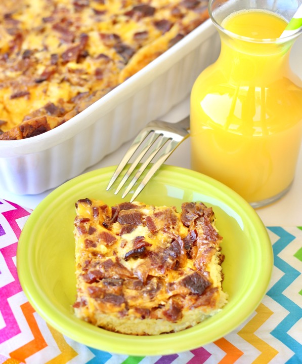Bacon and egg breakfast casserole piece in dish with orange juice on the side.