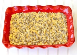 Breakfast casserole sausage and shredded cheddar cheese in casserole dish.