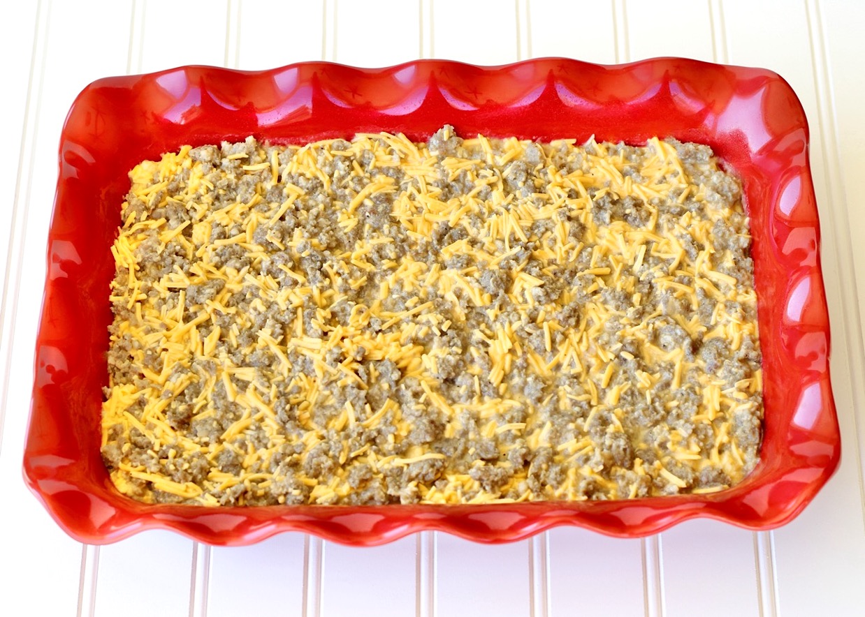 Breakfast casserole sausage and shredded cheddar cheese in casserole dish.