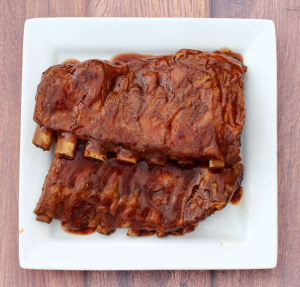 Cooked racks of ribs on plate covered in barbecue sauce.