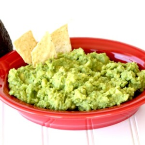 Two chips in a large red bowl of guacamole.