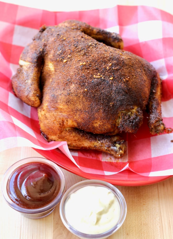 Cooked whole chicken covered with bbq rub and small dishes sauce on the side.