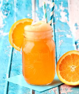 Orange punch in mason jar with orange slice and straws in glass.