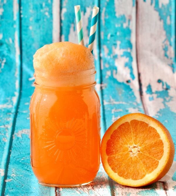 Orange punch in mason jar with straws and an orange to the side.