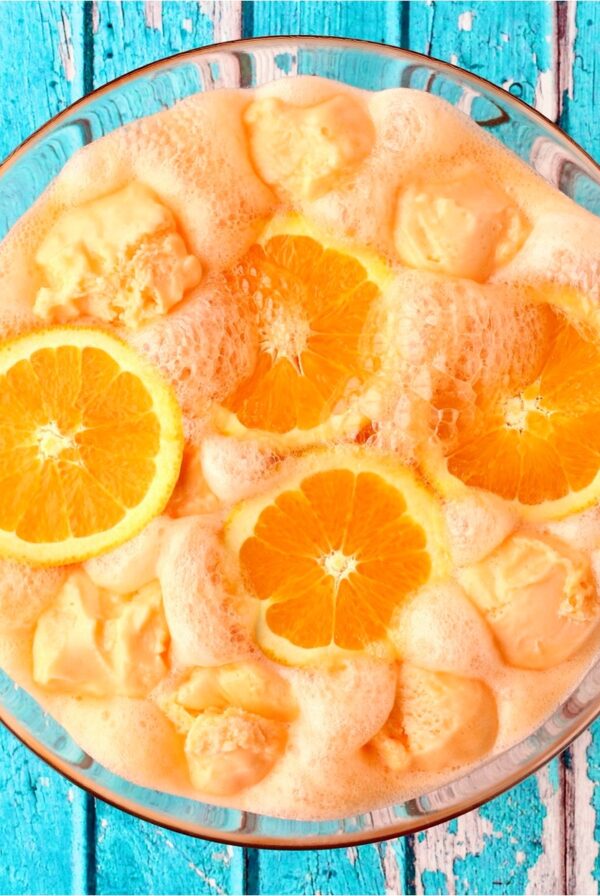 Orange Punch in glass punch bowl with scoops of sherbet and orange slices.