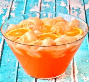 Orange punch in punch bowl with scoops of sherbet and orange slices floating on top.