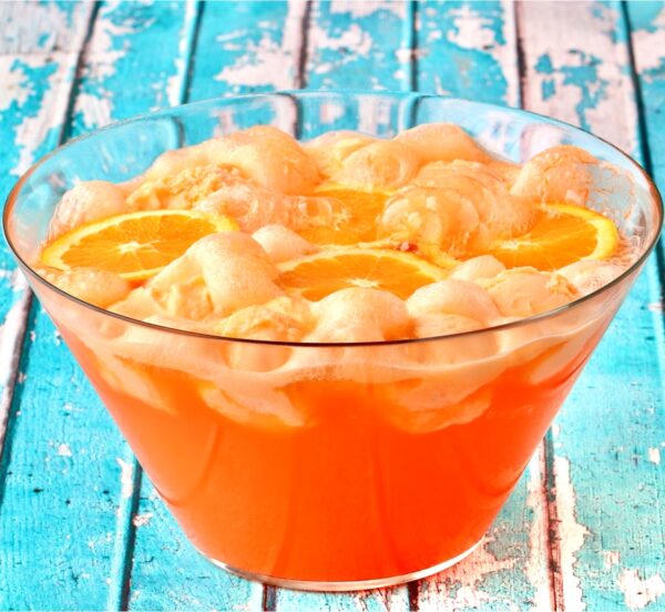 Orange punch in punch bowl with scoops of sherbet and orange slices floating on top.