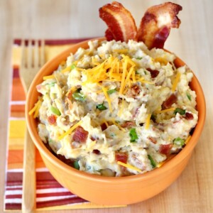 Orange bowl of smashed potatoes topped with cheese.