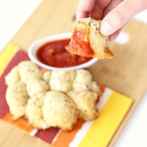 Person holding a piece of garlic parmesan bread with dip.