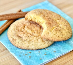 Two snickerdoodle cookies with cinnamon sugar, and cinnamon sticks to the side.