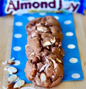 Three chocolate Almond Joy Cookies with coconut flakes and almonds on napkin.