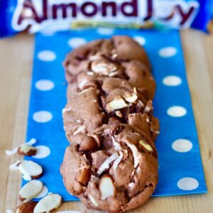 Three chocolate Almond Joy Cookies with coconut flakes and almonds on napkin.