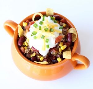 Taco soup in an orange bowl topped with sour cream and chopped green onions.
