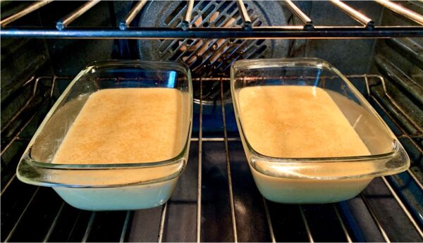 Two loaf pans of banana bread batter in an oven.