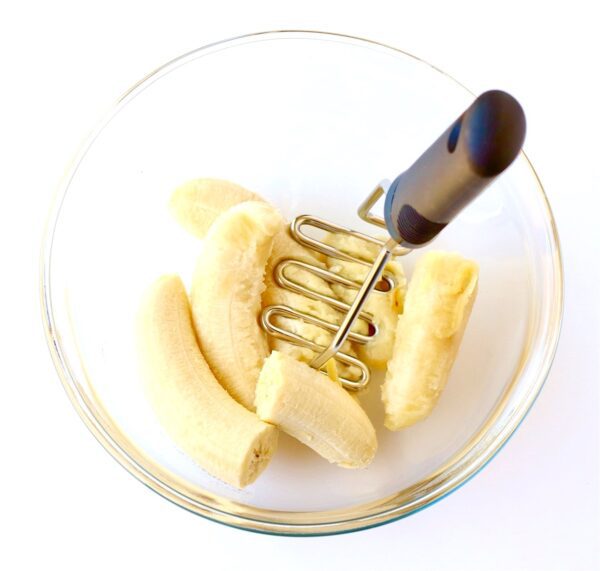 Masher mashing bananas in a bowl.