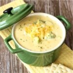 Cooked broccoli choose soup in a green bowl with shredded cheddar on top.