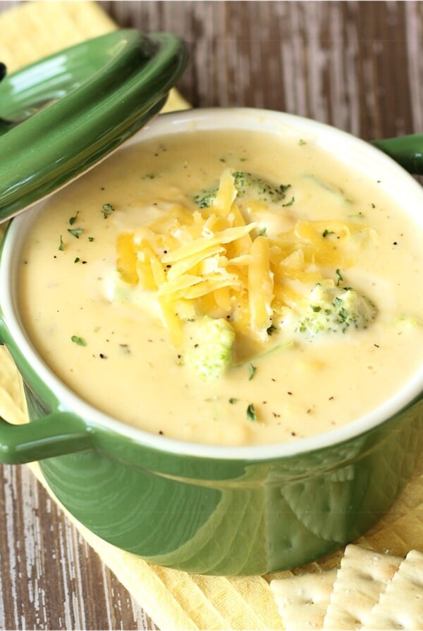 Cooked broccoli choose soup in a green bowl with shredded cheddar on top.