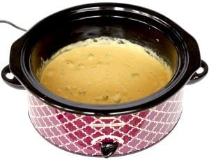 Broccoli cheese soup in a purple slow cooker.