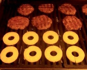 Burgers and pineapple slices on a grill.