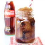 Frozen Coke Slushie in mason jar with straw and bottle of Coke in the background.