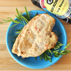 Grilled chicken on a blue plate with soy sauce bottle nearby.