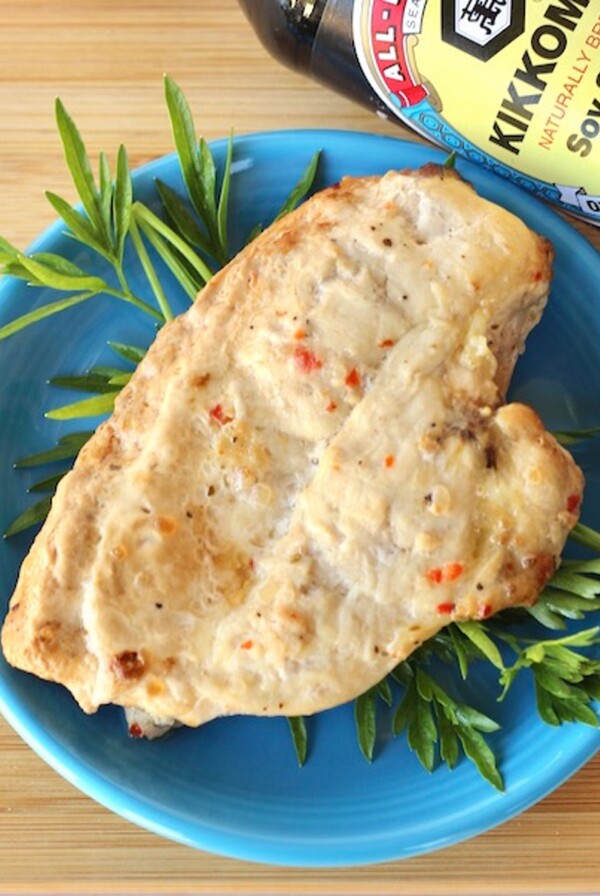 Grilled chicken on a blue plate with soy sauce bottle nearby.