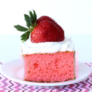 Slice of strawberry cake topped with frosting and a strawberry.